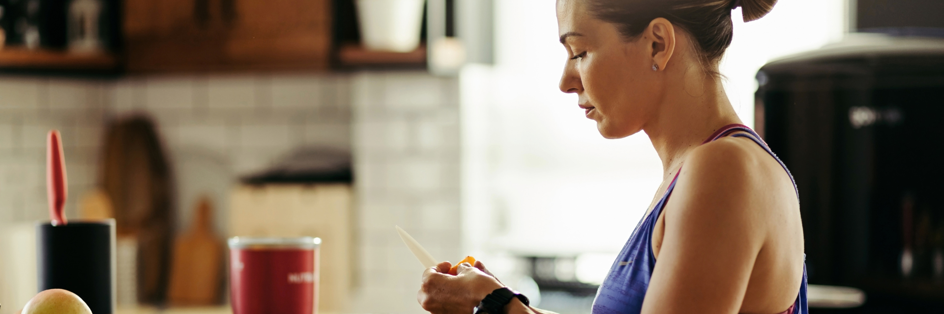 Mujer en ropa deportiva preparando alimentos saludables en la cocina de su casa.